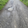 Buildwas Lane in Little Wenlock full of potholes and very worn road surface. There is a large puddle in one of the holes.