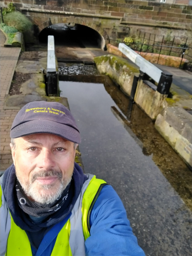 Cllr Tim Nelson in hi-vis and cap standing in front of Meretown Lock