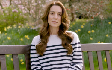 Princess of Wales sitting on a bench. There is grass and flowers behind her and she is wearing a white jumper with dark horizontal stripes.
